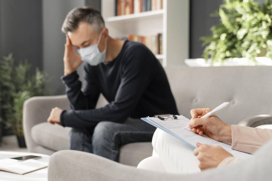 mid-shot-worried-man-with-mask-therapy-office-near-counselor